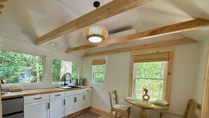 Una cocina con vigas de madera, un lavamanos, armarios, una ventana con vistas al verdor y una pequeña mesa con sillas.