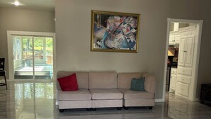 Ein geräumiges Wohnzimmer mit einem hellen Sofa, einem großen abstrakten Gemälde und einem glänzenden Boden.