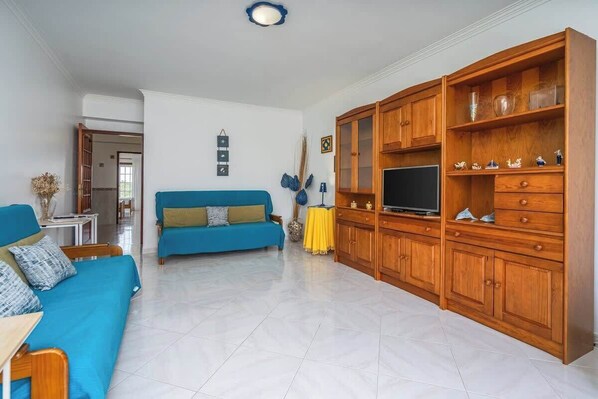 Una sala de estar con un sofá azul, armarios de madera, un televisor y una mesa amarilla.