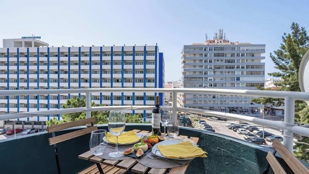 Un balcone con un tavolo apparecchiato per due persone, affacciato su un'area di parcheggio e edifici.