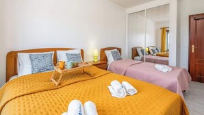 Camera d'hotel con due letti, ciascuno con testiera in legno, un grande specchio e un comodino in legno con una lampada.