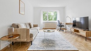 Ein modernes Wohnzimmer mit einer Couch, einem Couchtisch, einem Fernseher und einem großen Fenster.
