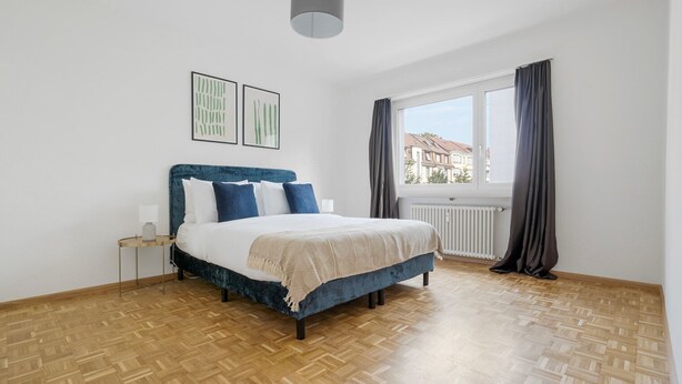 Ein Schlafzimmer mit einem Bett, einem Nachttisch, einem Fenster mit Vorhängen und einer Heizung.