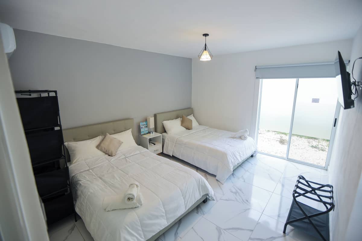 Habitación de hotel con dos camas, una mesita, una silla, televisor y ventana con vistas.