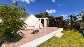 A tented outdoor area with a stone wall, a bench, and a grassy lawn.