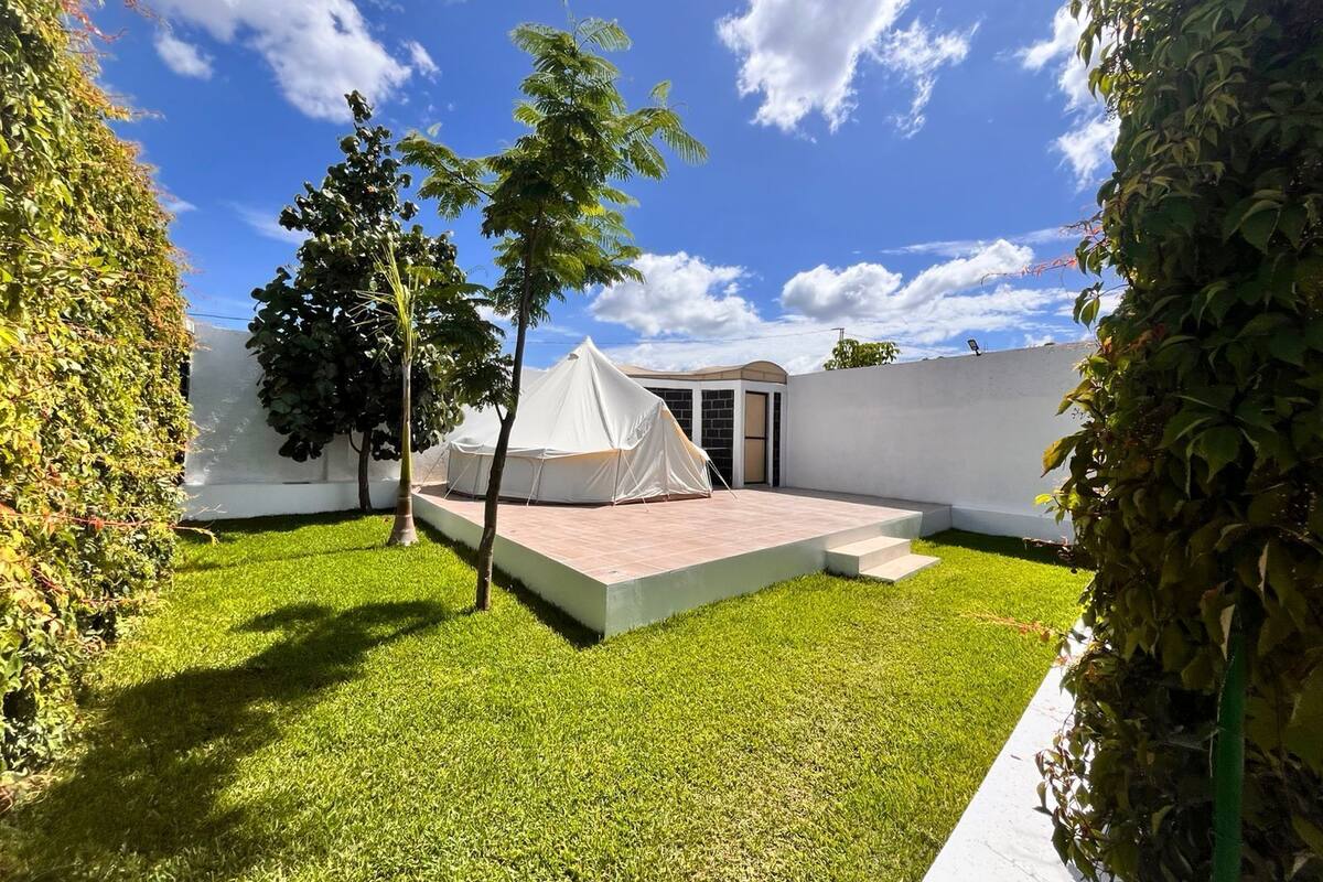 Un petit espace extérieur clos, comprenant une tente blanche, une plateforme pavée et une pelouse.