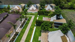 Luchtbeeld van een resort met meerdere tenten in de stijl van bungalows, een verharde centrale pad en verzorgde beplanting.