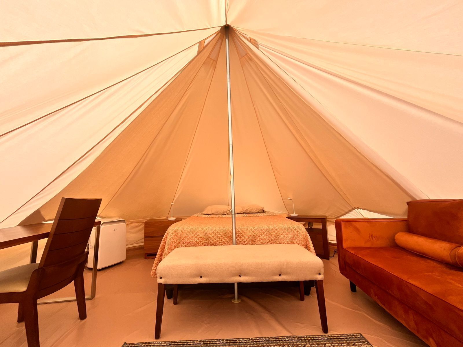 A tent with a bed, a wooden chair, a small table, and a sofa.