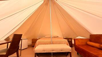A tent with a bed, a wooden chair, a small table, and a sofa.