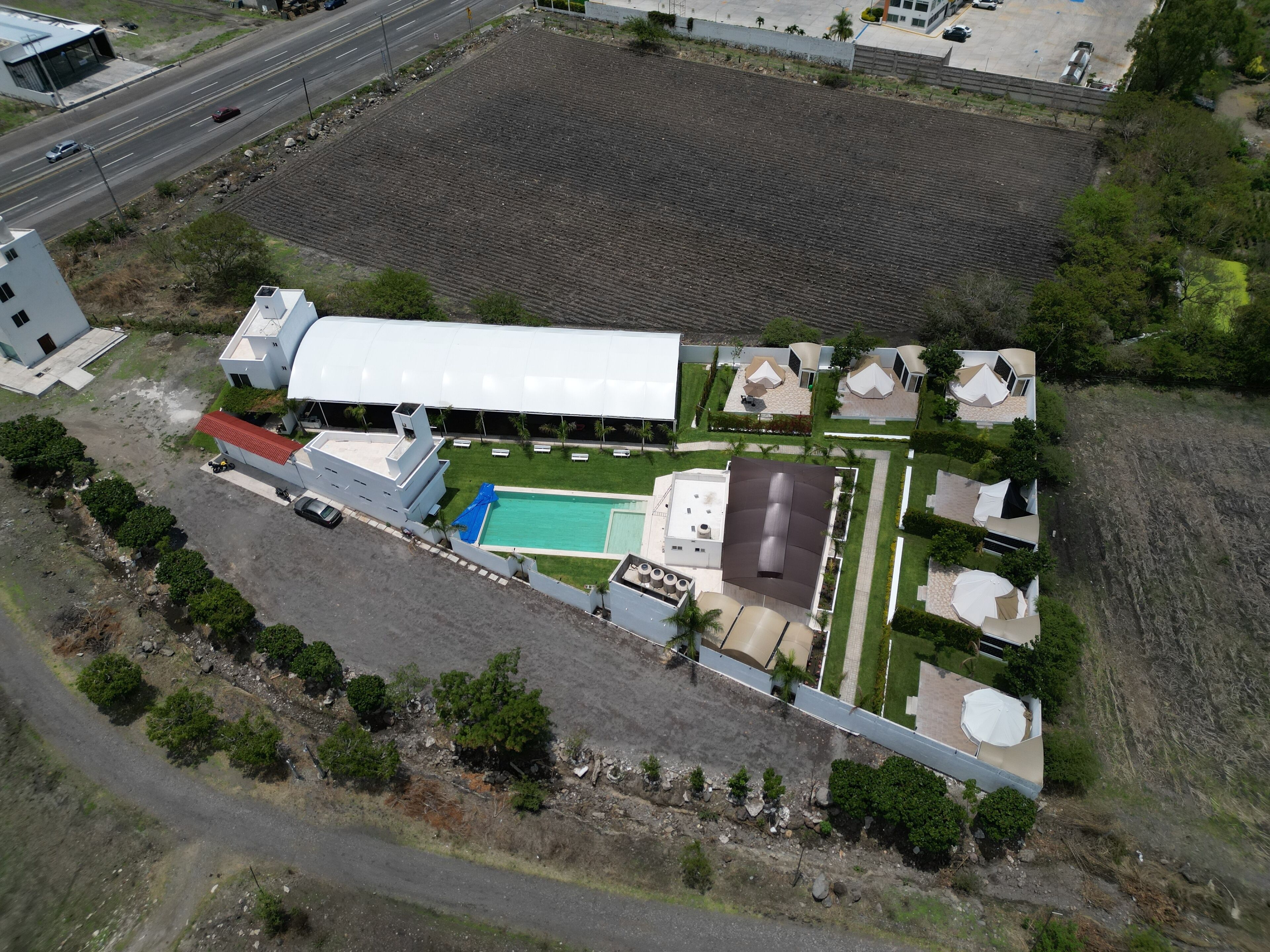 Vista aérea de un edificio grande con piscina, cancha de tenis y varias construcciones más pequeñas.