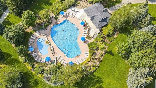 An aerial view of a resort with a large central swimming pool, multiple smaller pools, and a well-maintained lawn with lounge areas.