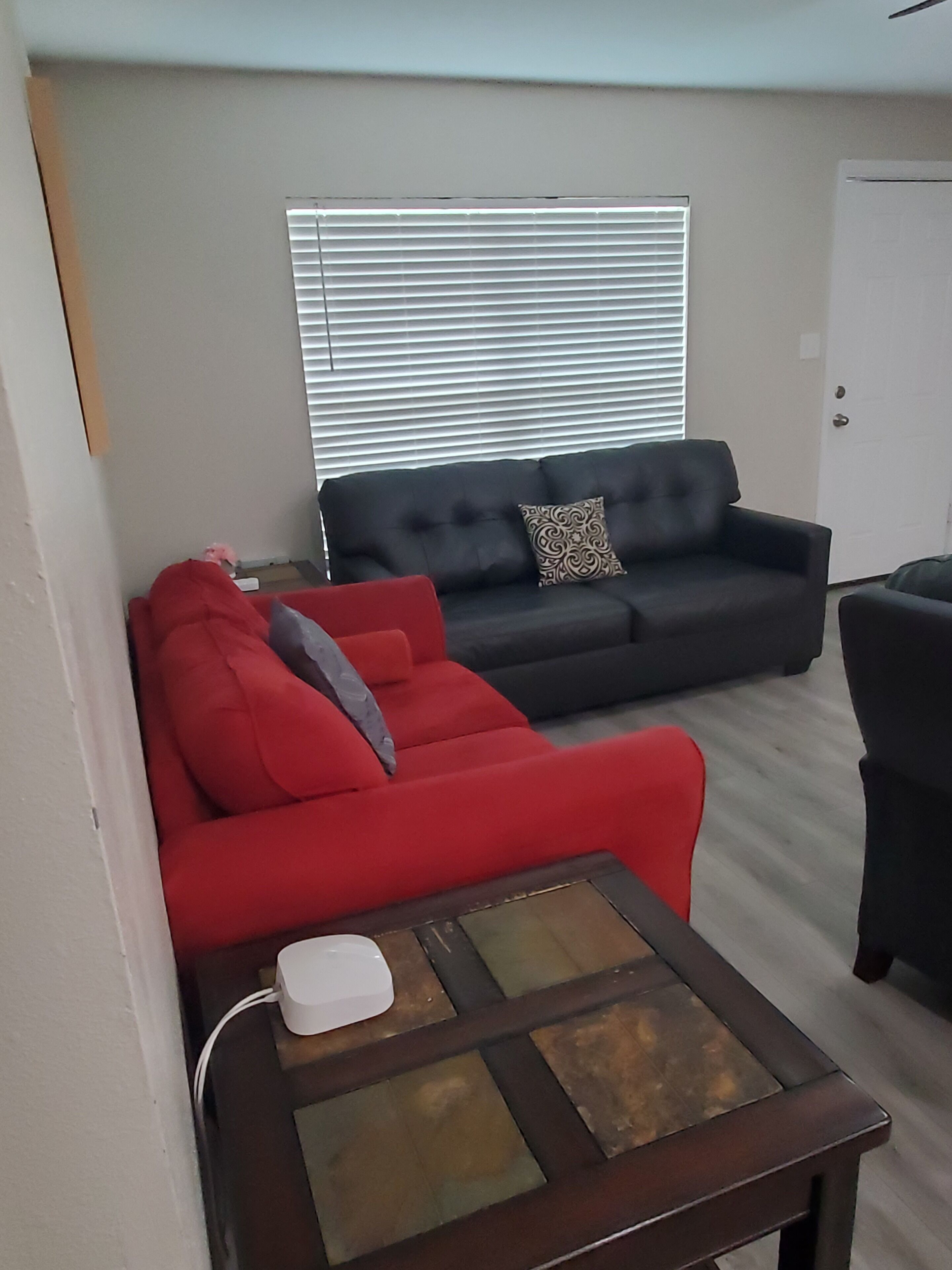 Un salon avec un canapé rouge, un canapé noir et une table basse dont le plateau est en verre.