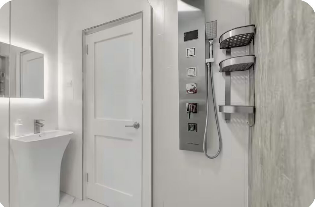 Une salle de bain moderne avec un lavabo blanc, une porte et un panneau de commande de douche fixé au mur.