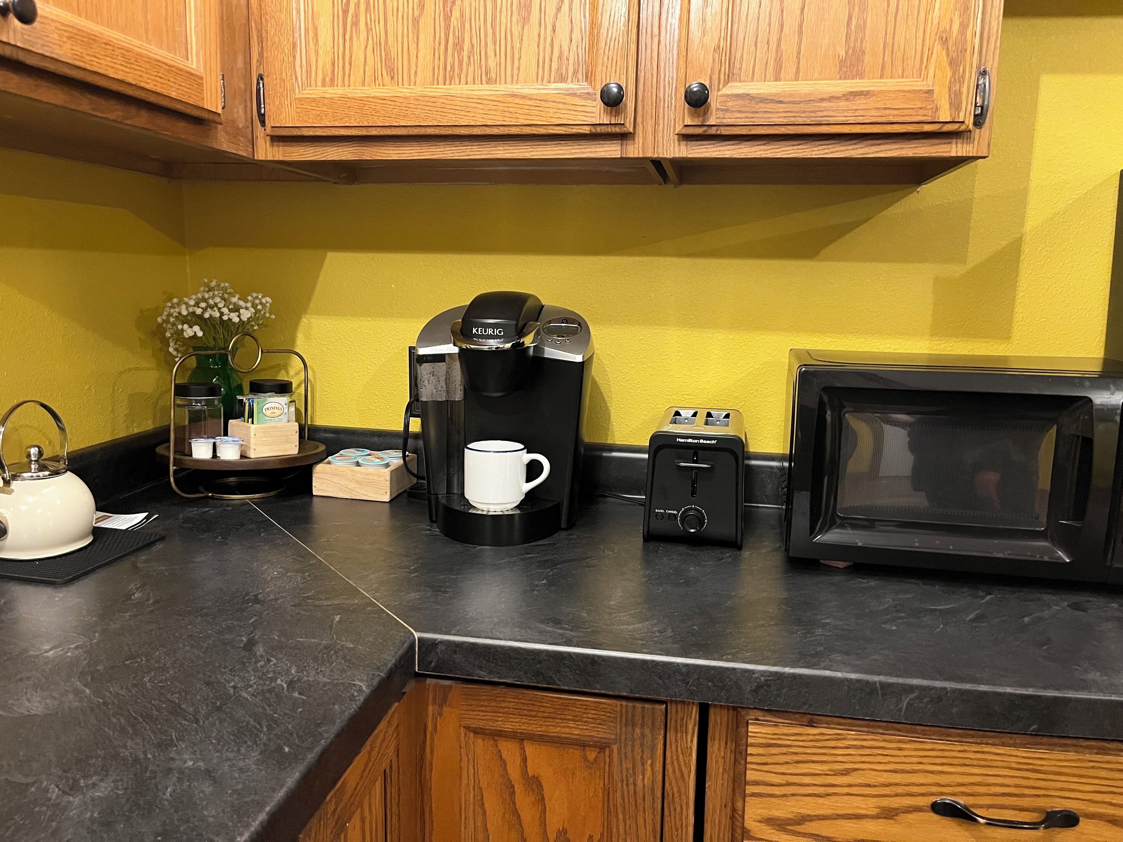 A kitchen with wooden cabinets, a coffee maker, a toaster, a kettle, and a microwave.