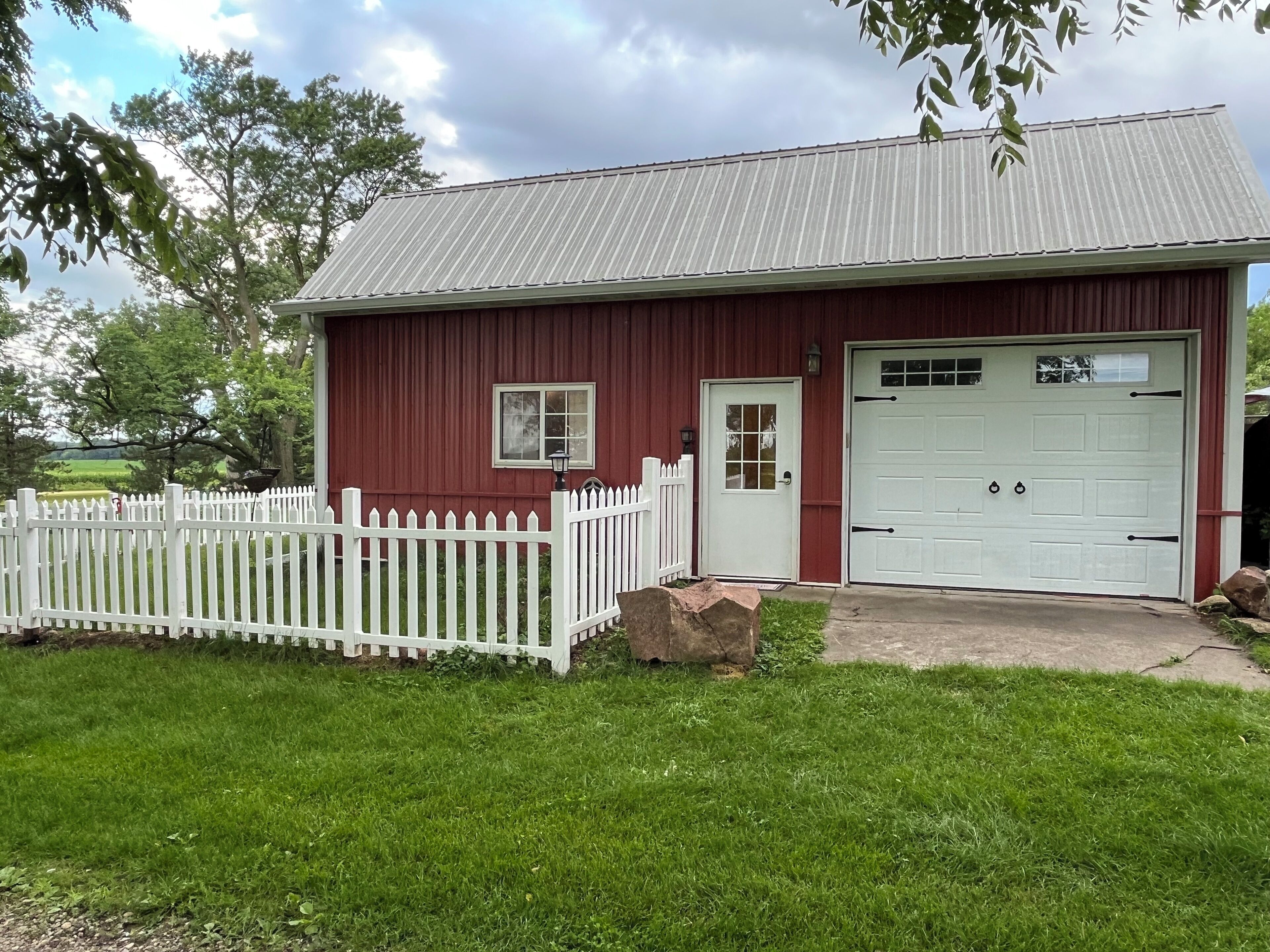 A red building with a white garage door, a white picket fence, and a small window.