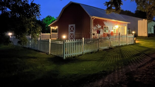 A barn with a white picket fence, a covered porch, and a red exterior. - The Little Red Barn (Cedar Falls)