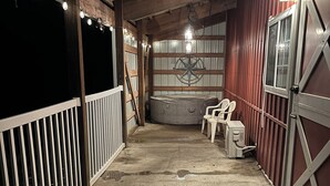 A stable with a concrete floor, white railings, and a red wall. There are two white plastic chairs and a lantern hanging from the ceiling. - The Little Red Barn (Cedar Falls)