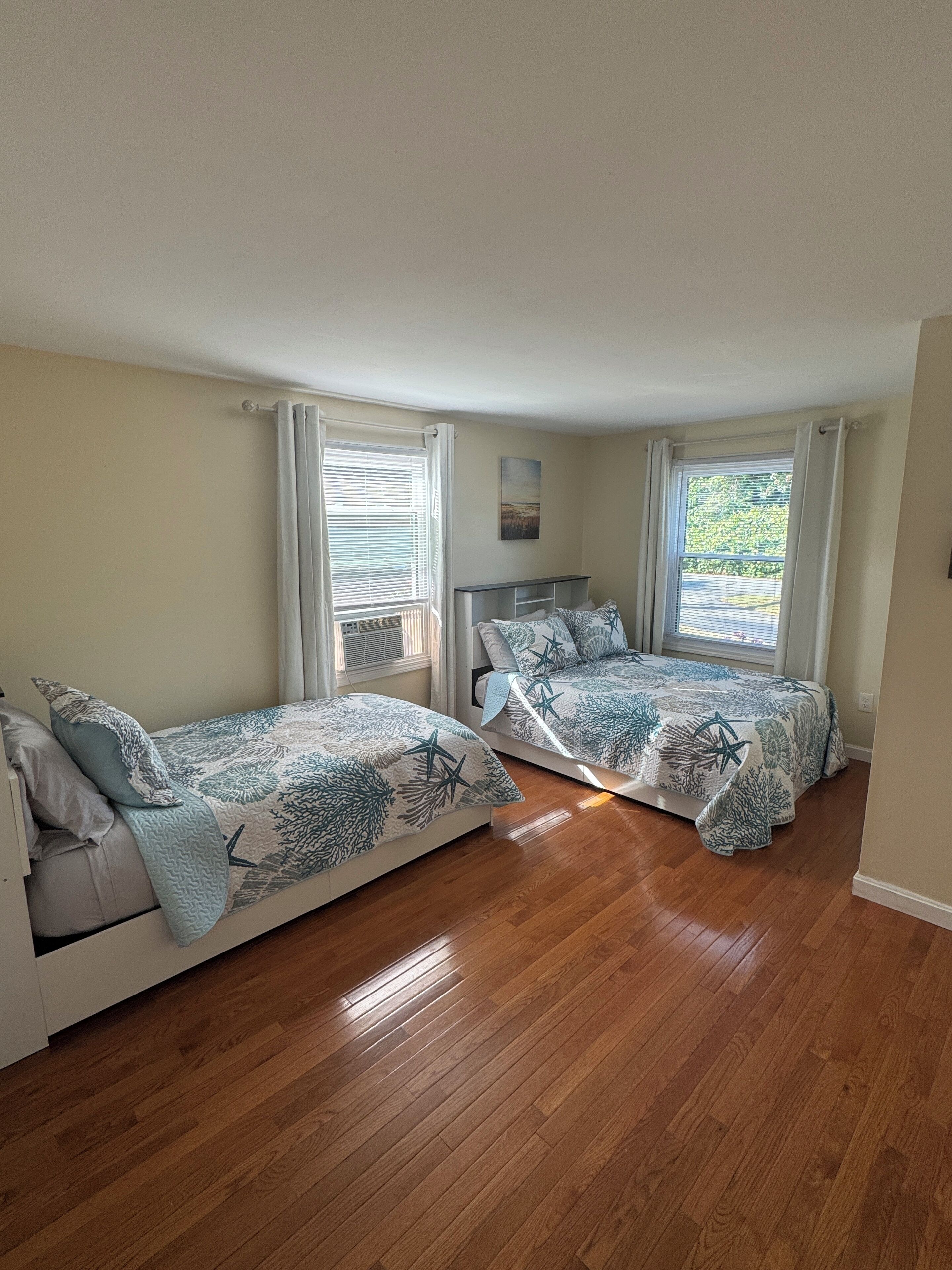 A bedroom with two single beds, wooden flooring, and a window with curtains.