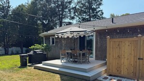 Ein Garten mit Terrasse, Sitzgelegenheit im Freien, Grill und Holzzaun.