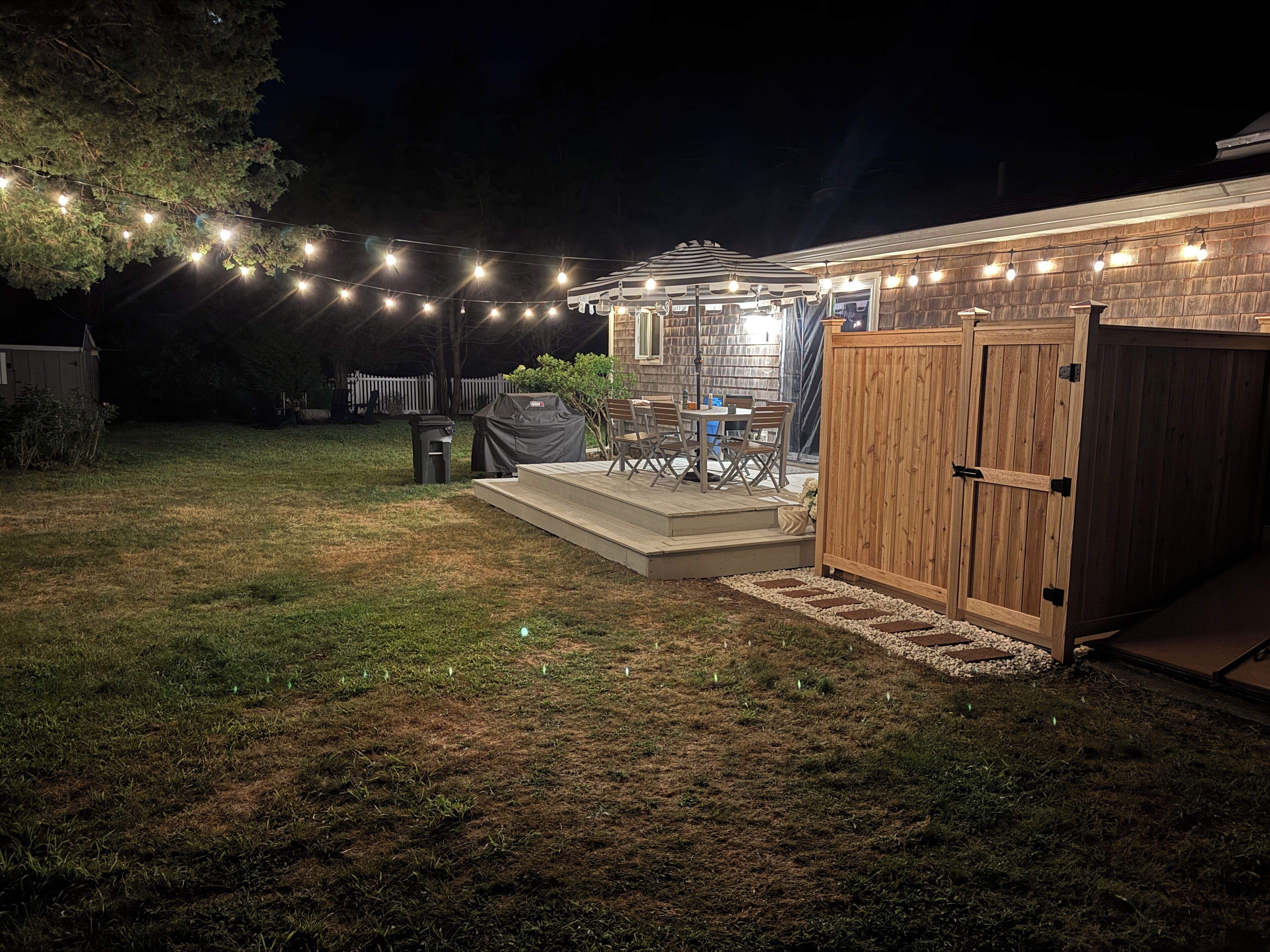 A backyard with a covered patio area, a wooden deck, and string lights.