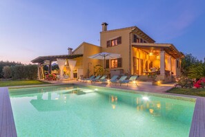 Una casa moderna con piscina, mobiliario exterior y un patio cubierto.