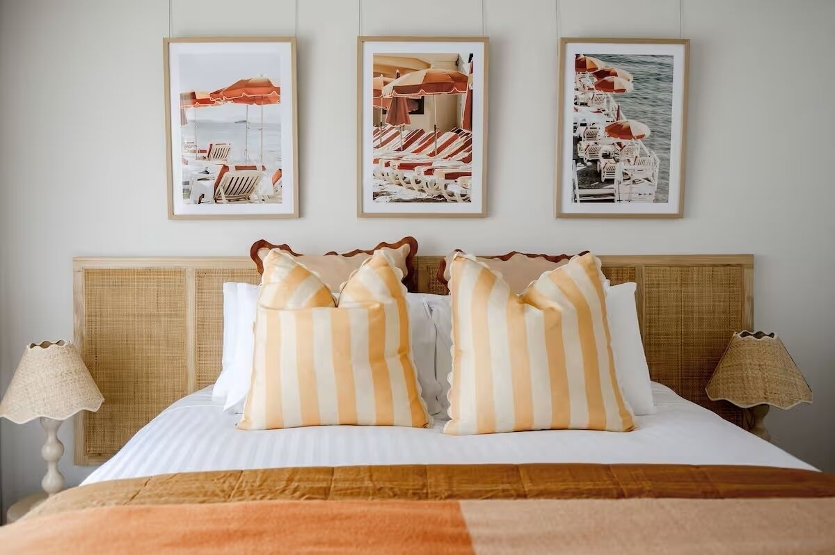A neatly made bed with striped pillows, framed beach photos on the wall, and two bedside lamps.