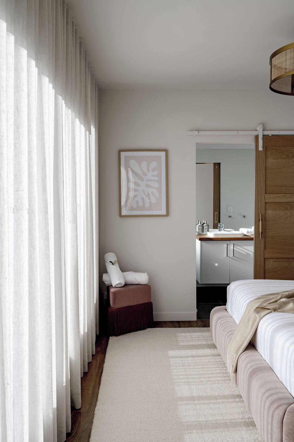 A bedroom with a bed, a chair, a small table with toiletries, a mirror, and a door leading to a bathroom.