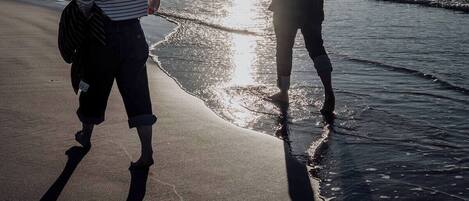 Twee mensen wandelen over een strand, met een ondergaande zon op de achtergrond.