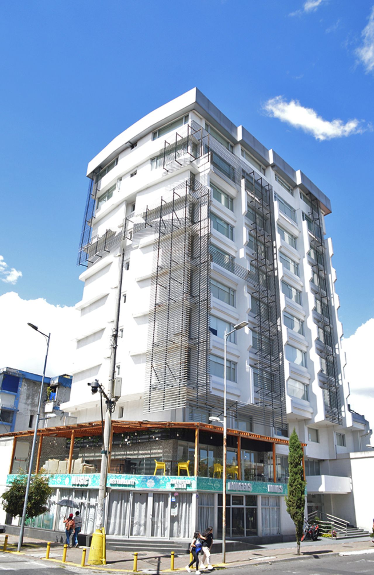 Un edificio de varios pisos con un diseño arquitectónico moderno, que presenta un elemento vertical destacado y un espacio comercial en planta baja con escaparate.