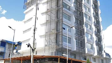 Un edificio de varios pisos con un diseño arquitectónico moderno, que presenta un elemento vertical destacado y un espacio comercial en planta baja con escaparate.