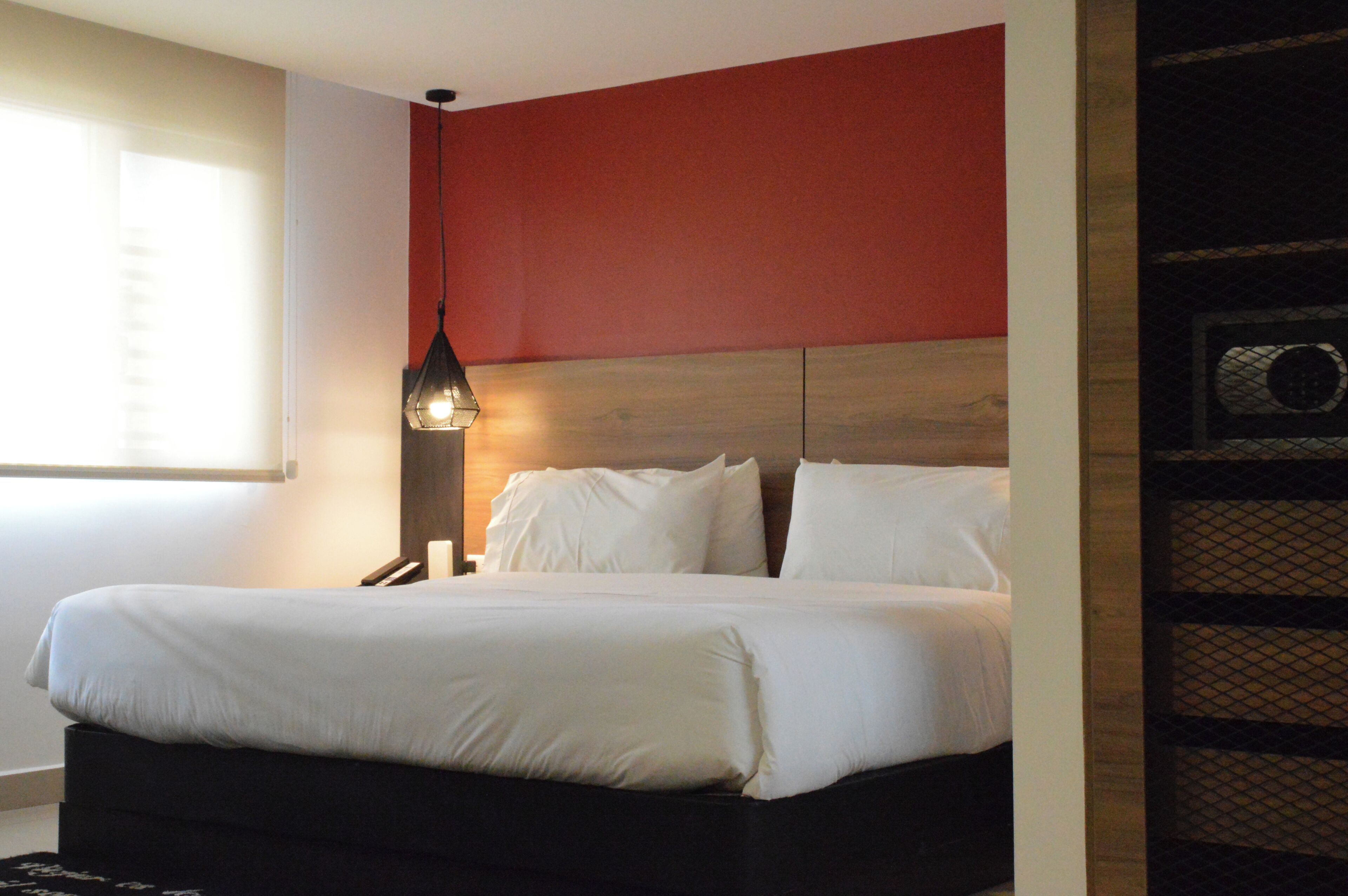 A hotel room with a bed, a nightstand, a lamp, and a window with blinds.
