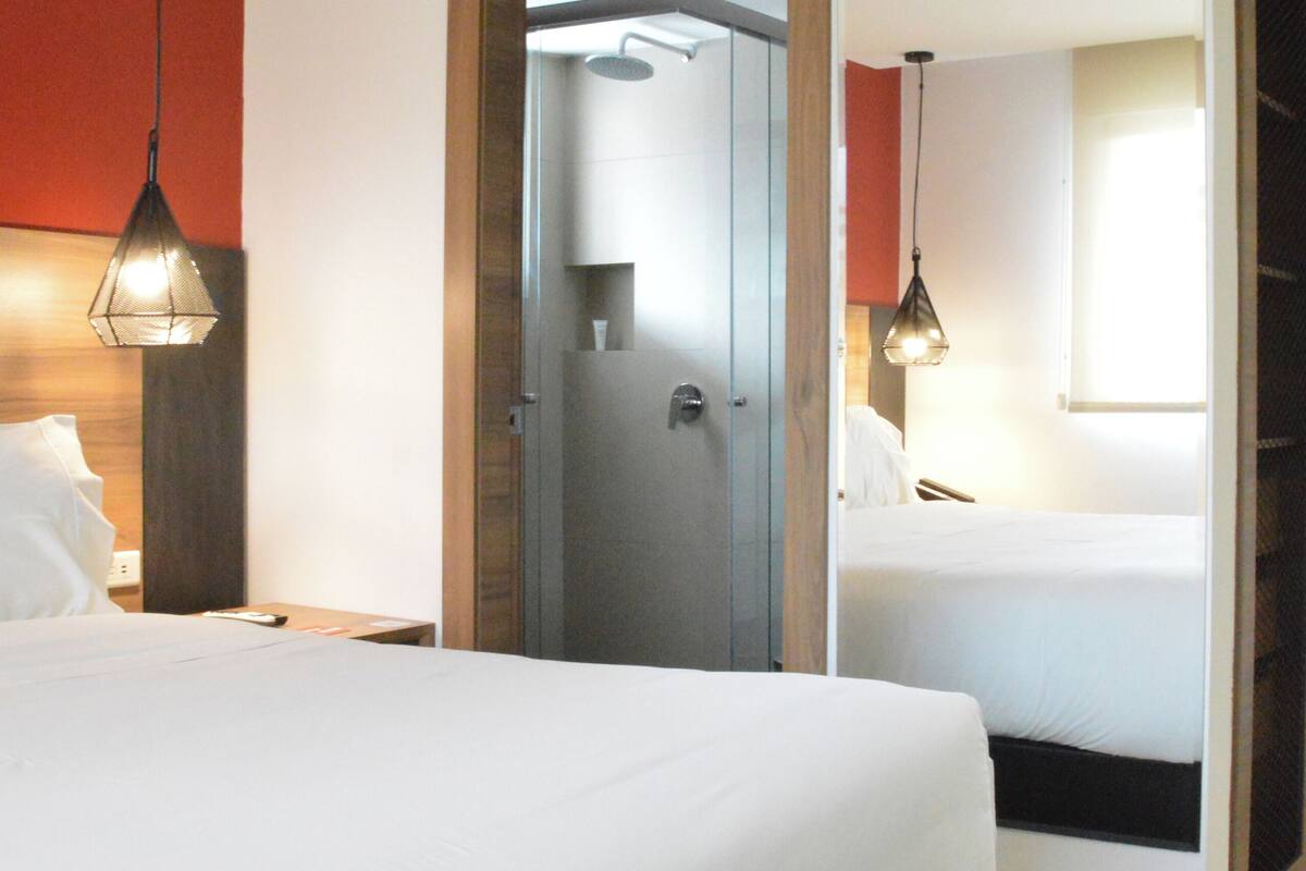 A hotel room with a large bed, a desk, a chair, a wardrobe, and a bathroom visible through an open door.