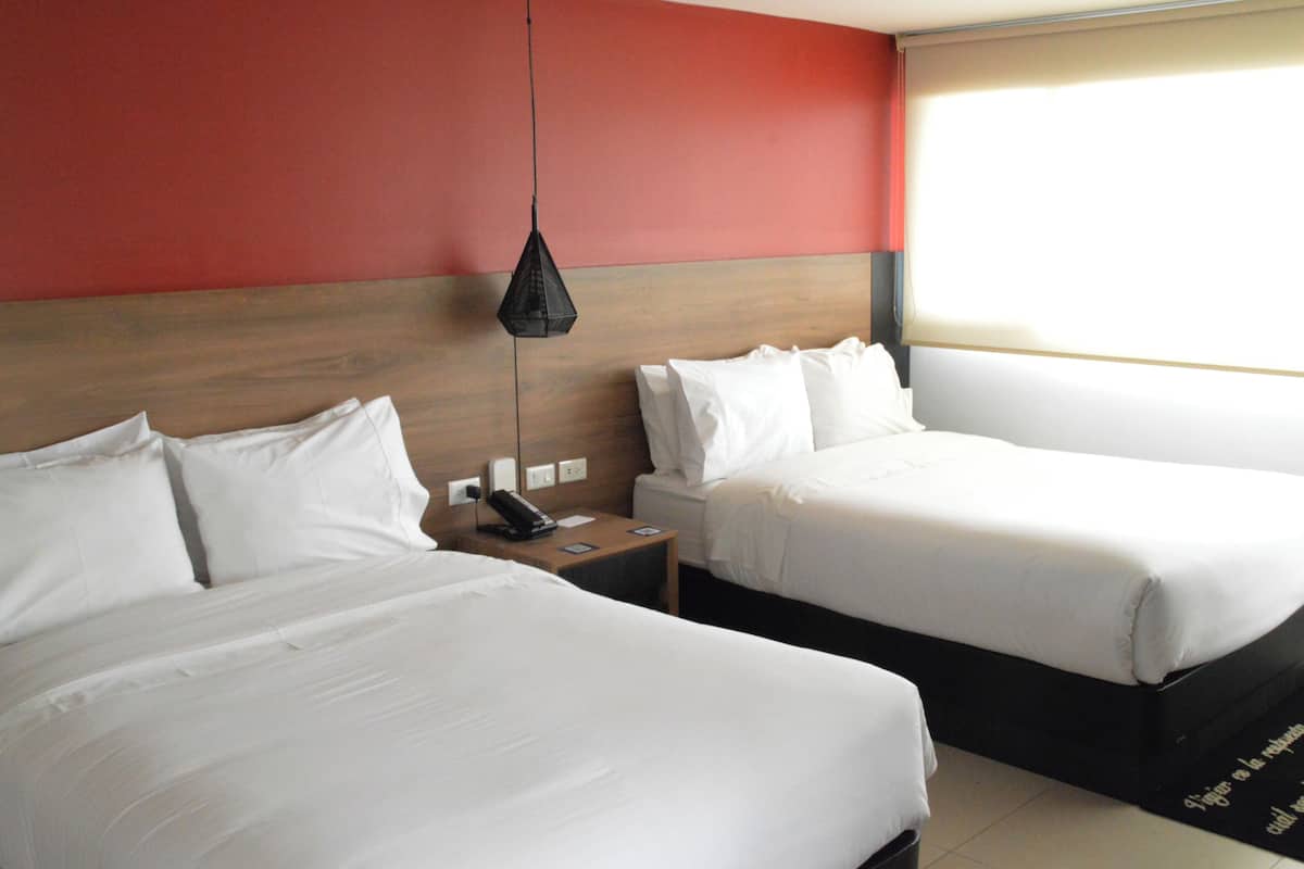 A hotel room with two beds, a wooden headboard, a bedside table with a phone, and a hanging light fixture.