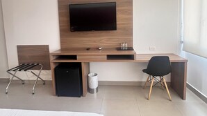 Une chambre d’hôtel moderne avec un bureau en bois, un téléviseur à écran plat, une chaise noire, un petit haut-parleur noir et une poubelle.