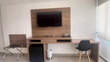 A modern hotel room with a wooden desk, a flat-screen TV, a black chair, a small black speaker, and a waste bin.