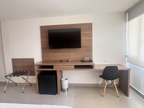 A modern hotel room with a wooden desk, a flat-screen TV, a black chair, a small black speaker, and a waste bin. - The Place Hotel (Quito)