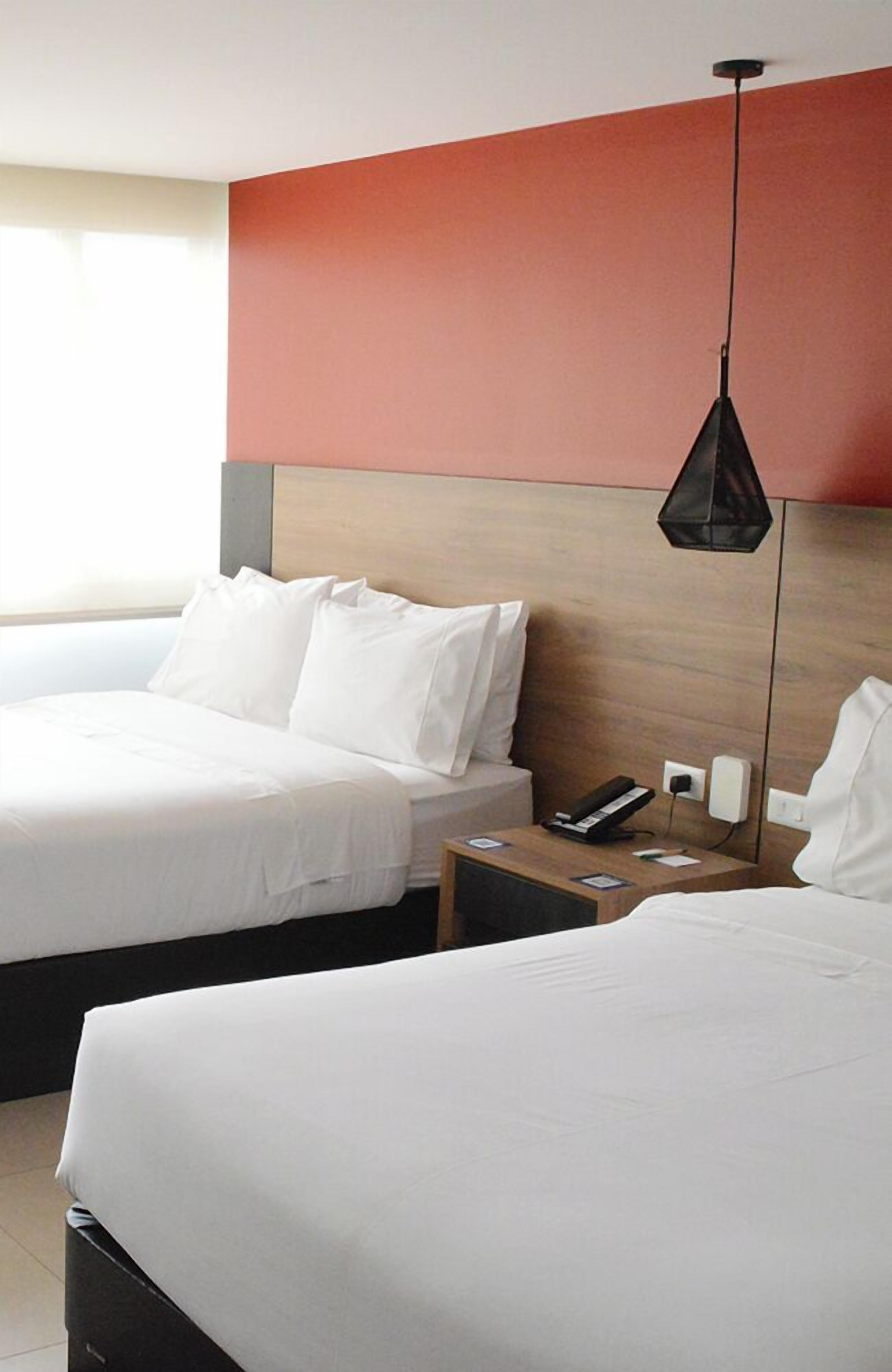 Une chambre d’hôtel avec deux lits, une table de chevet avec un téléphone et une lampe suspendue.