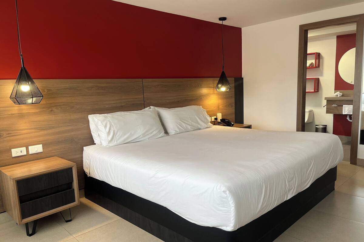 A modern hotel room with a large bed, bedside tables, and a red accent wall.