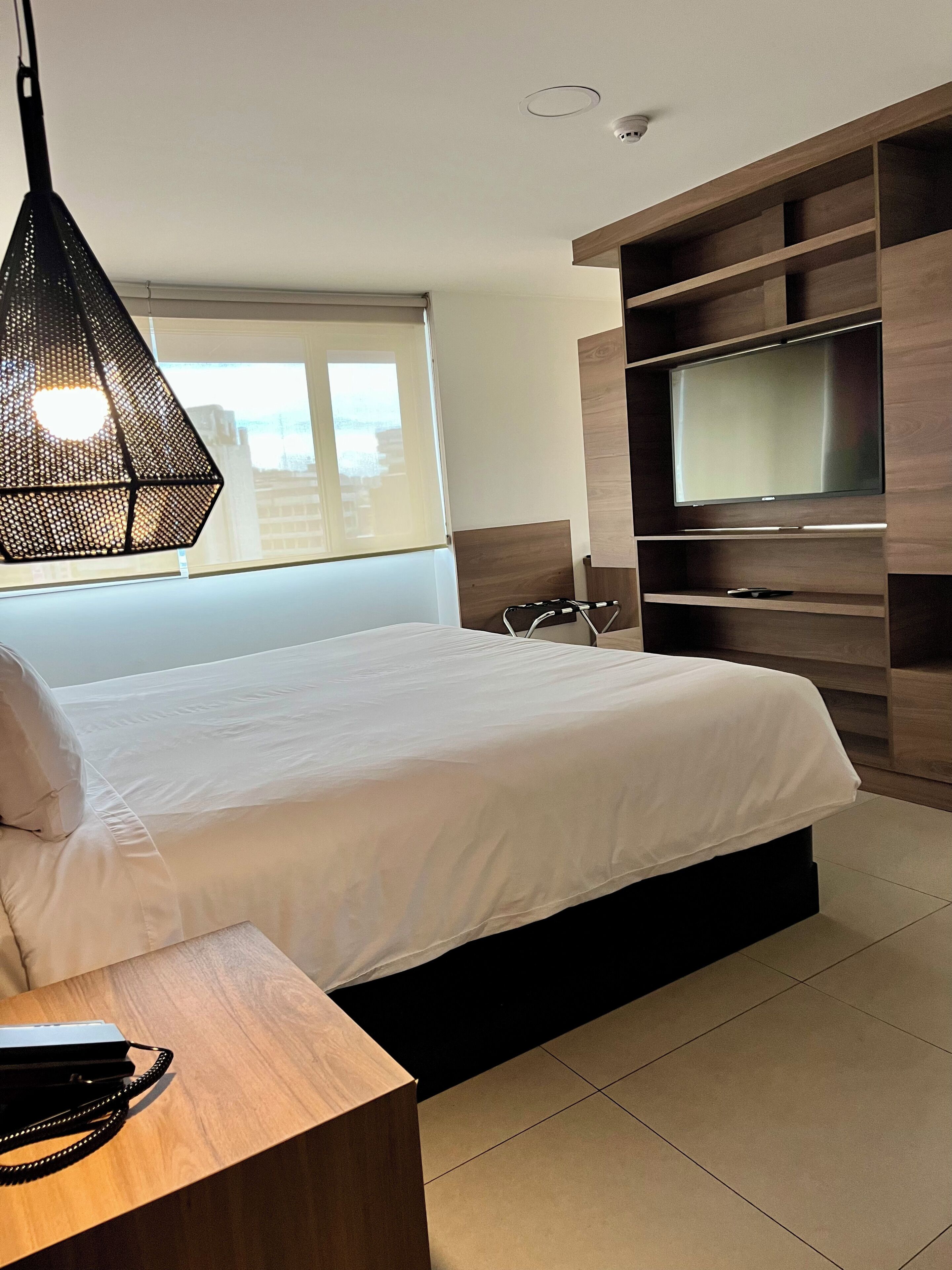 Ein modernes Schlafzimmer mit Bett, Fernseher, einem Holztisch und einer Pendelleuchte.