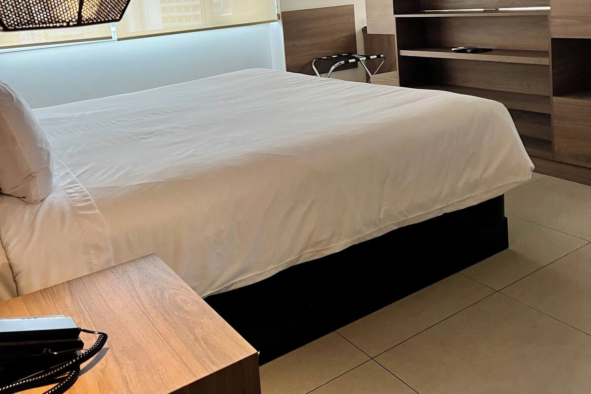 A modern bedroom with a bed, a TV, a wooden desk, and a hanging light fixture.