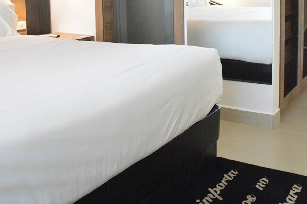 A hotel room with a bed, a wardrobe, a mirror, and a door leading to another room.