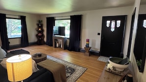 Ein Wohnzimmer mit einem schwarzen Sofa, einer Lampe, einem Fernseher und einem Holztisch.