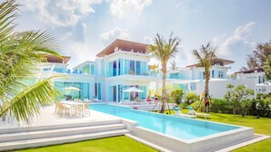 A modern multi-story house with a swimming pool, outdoor seating, and lush greenery.