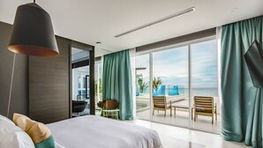 A modern bedroom with a large bed, a view of the beach, and a balcony with seating.