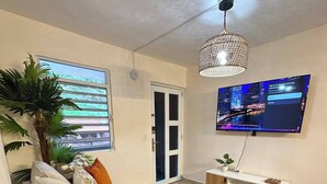 Una sala de estar moderna con un sofá, una mesa de centro, un televisor montado en la pared, una planta en maceta y un ventanal corredizo que da a un balcón.