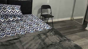 Un dormitorio con cama, una silla y un ventanal pequeño.