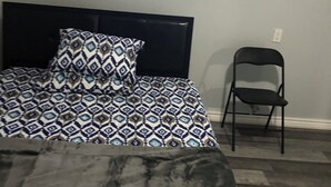 Un dormitorio con una cama, un cojín estampado, una silla negra y una ventana pequeña.