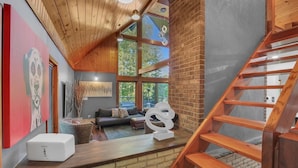 A loft-style living area with a wooden ceiling, a brick wall, and a staircase.