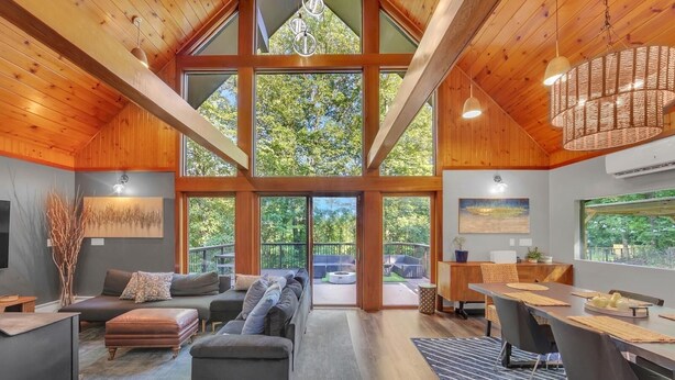 A spacious room with a large window, a sofa, a dining table, and a chandelier.