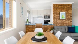 A modern kitchen with white cabinets, a brick accent wall, and a dining area with a wooden table and white chairs.